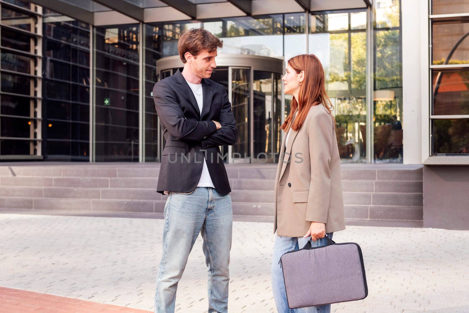 business man and woman standing outside of an office building talking to each other, they are wearing casual clothes