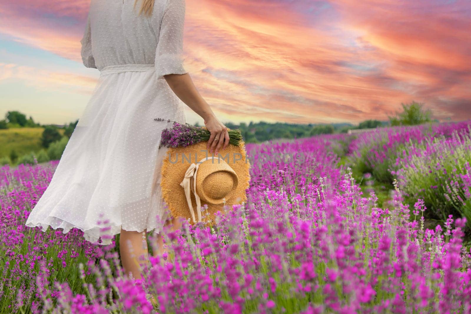 Woman holding lavender bouquet and hat in hands in lavender field.