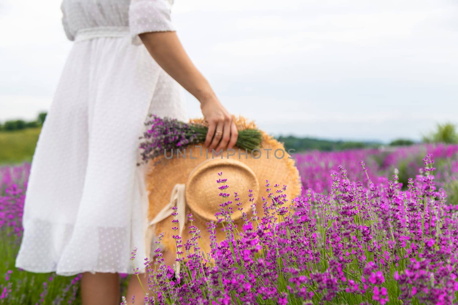 Woman holding lavender bouquet and hat in hands in lavender field.