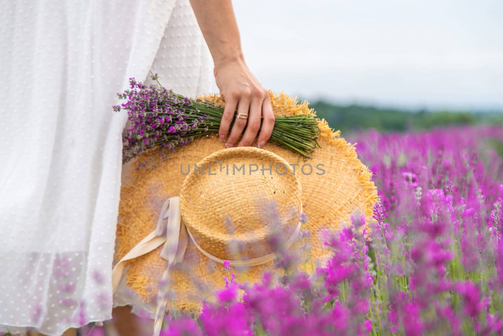 Woman holding lavender bouquet and hat in hands in lavender field.