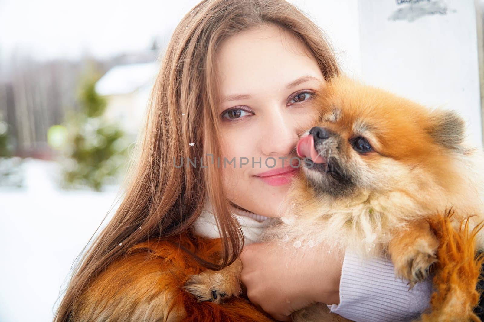 Girl shares affection with her fluffy Pomeranian in a winter wonderland, showcasing their bond in the snow.