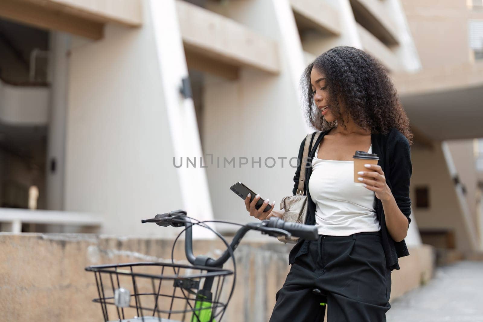Pausing for a moment, a woman enjoys her coffee as she checks her phone, seamlessly blending urban life with sustainable commuting on her bicycle.