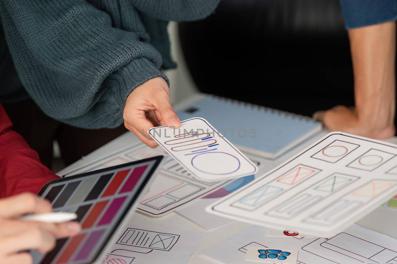 A team member presents a mobile layout prototype to colleagues, highlighting the design elements on a conference table filled with sketches and digital inspirations.