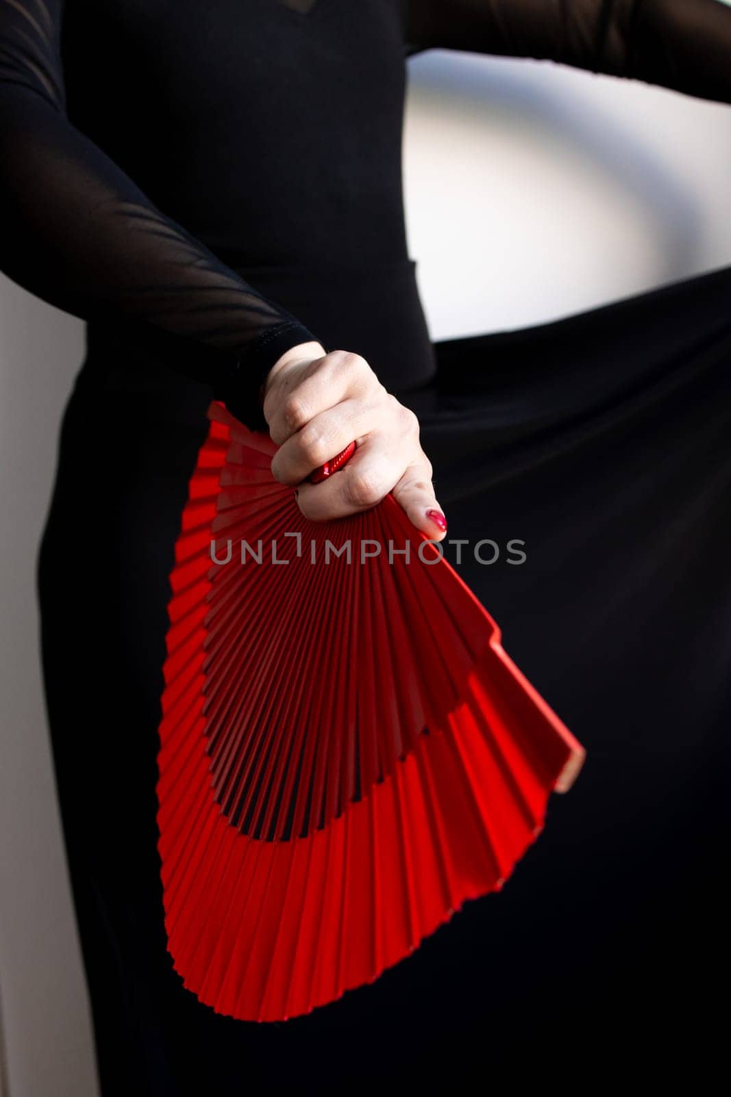 Elegant female holding red fan in black attire.