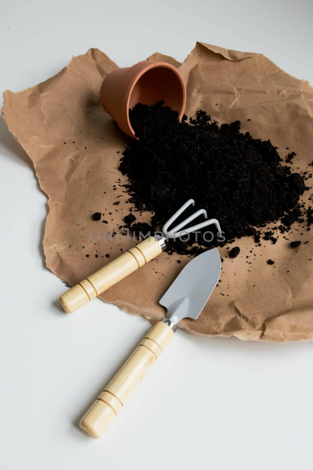 Brown paper with spilled soil and gardening tools on white background.
