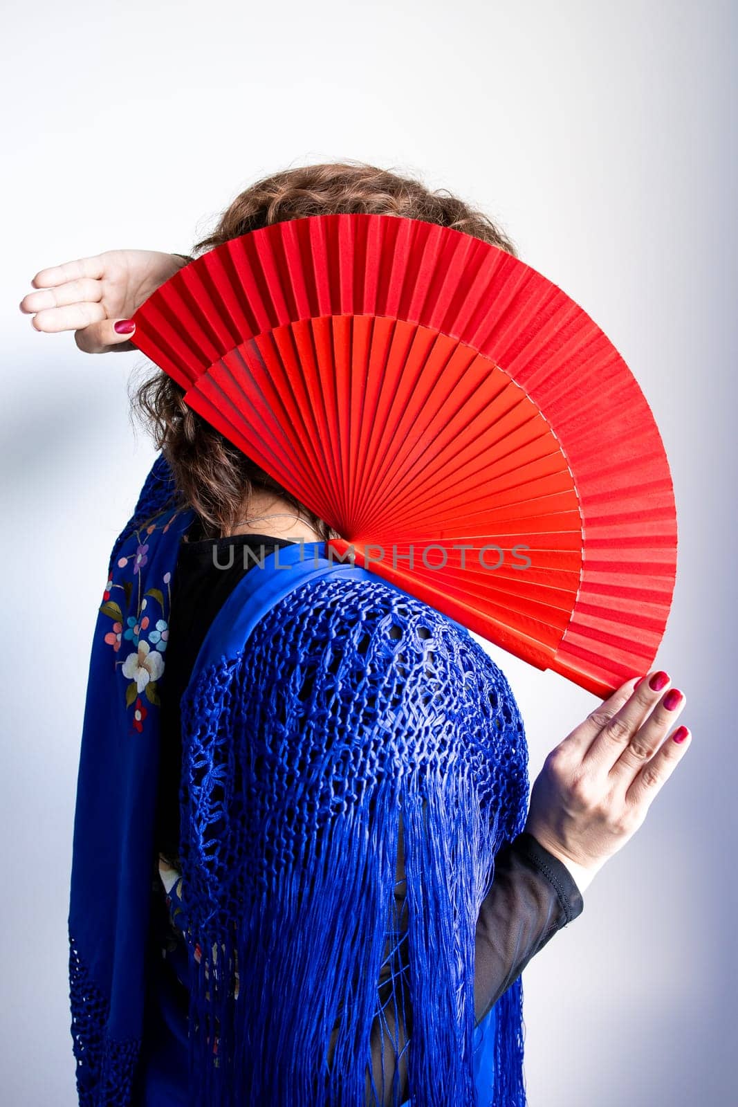 Female in traditional spanish attire with red fan covering face.