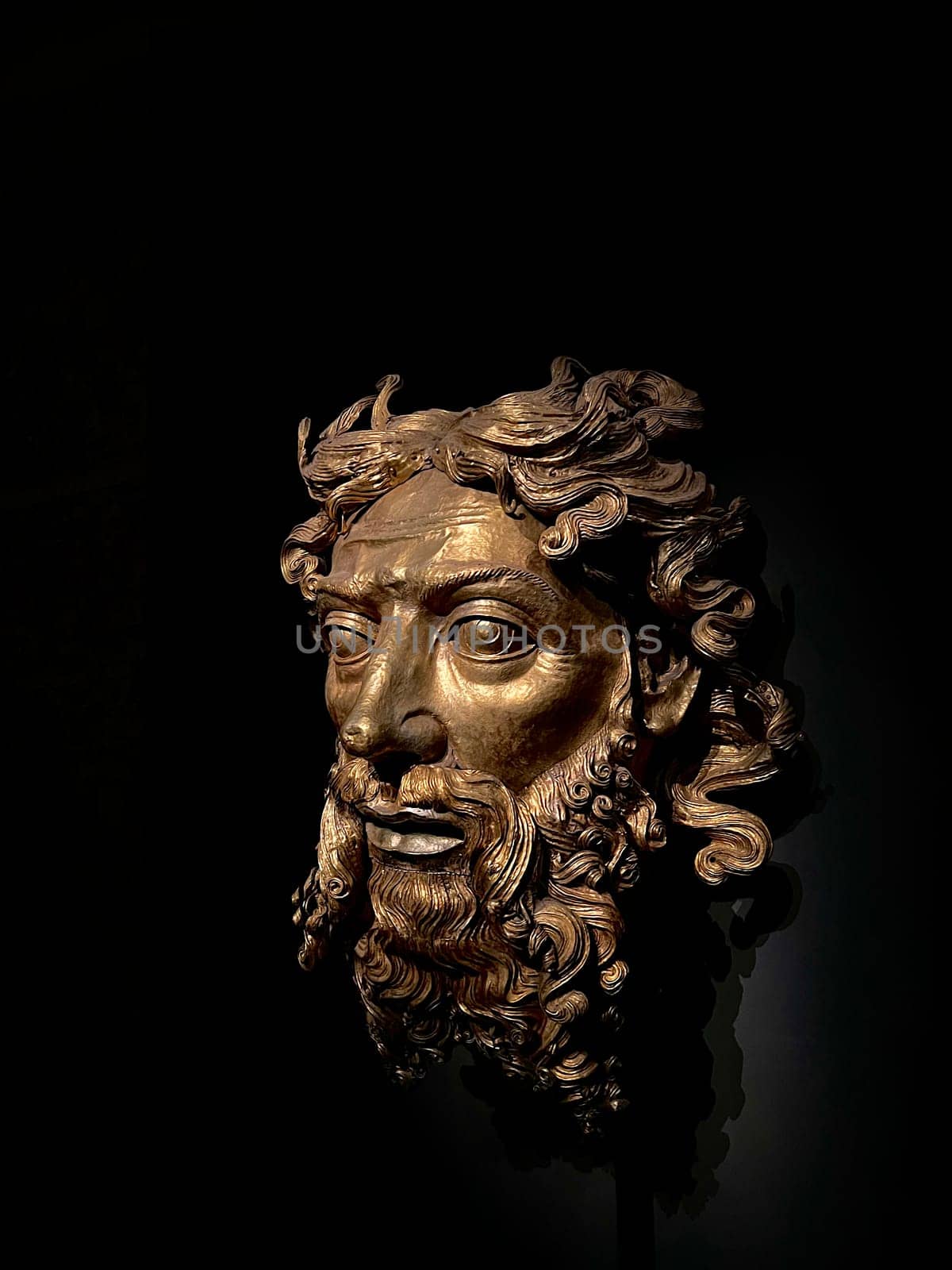 08.11.2022 Milan: Golden Sculpture of God the Father, Duomo Museum. A striking close-up of the gilded bronze sculpture God the Father (Padre Eterno), housed in the Museo del Duomo in Milan, Italy. The intricately detailed artwork features a solemn face with deep-set eyes, flowing curls, and a majestic beard, exuding divine authority. The dramatic lighting enhances the rich golden tones, set against a deep black background, creating a powerful contrast. This historical masterpiece reflects