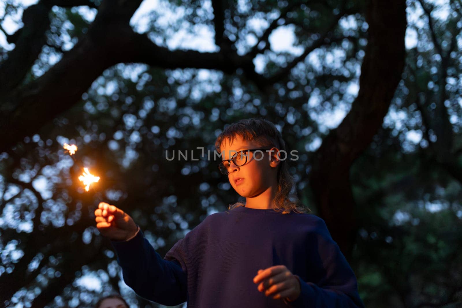 Young boy holding sparkling bengal light in the woods at dusk