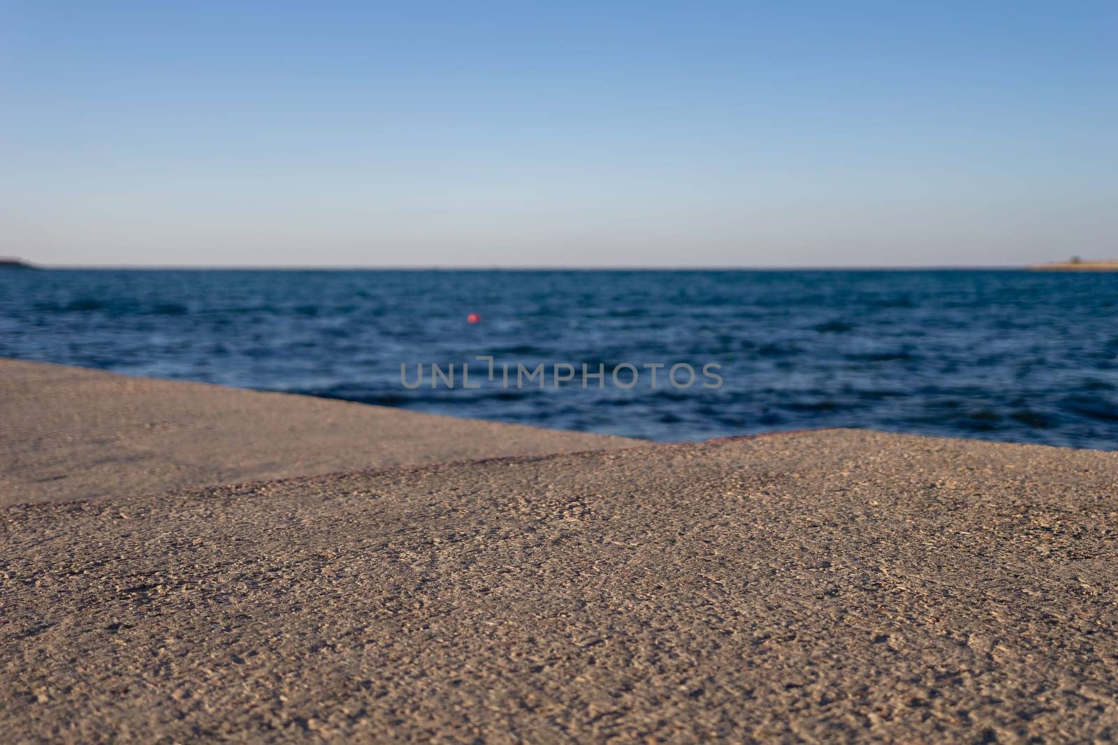 A sandy beach stretches towards a calm, blue ocean under a clear sky. The water gently laps at the shore, creating small waves.