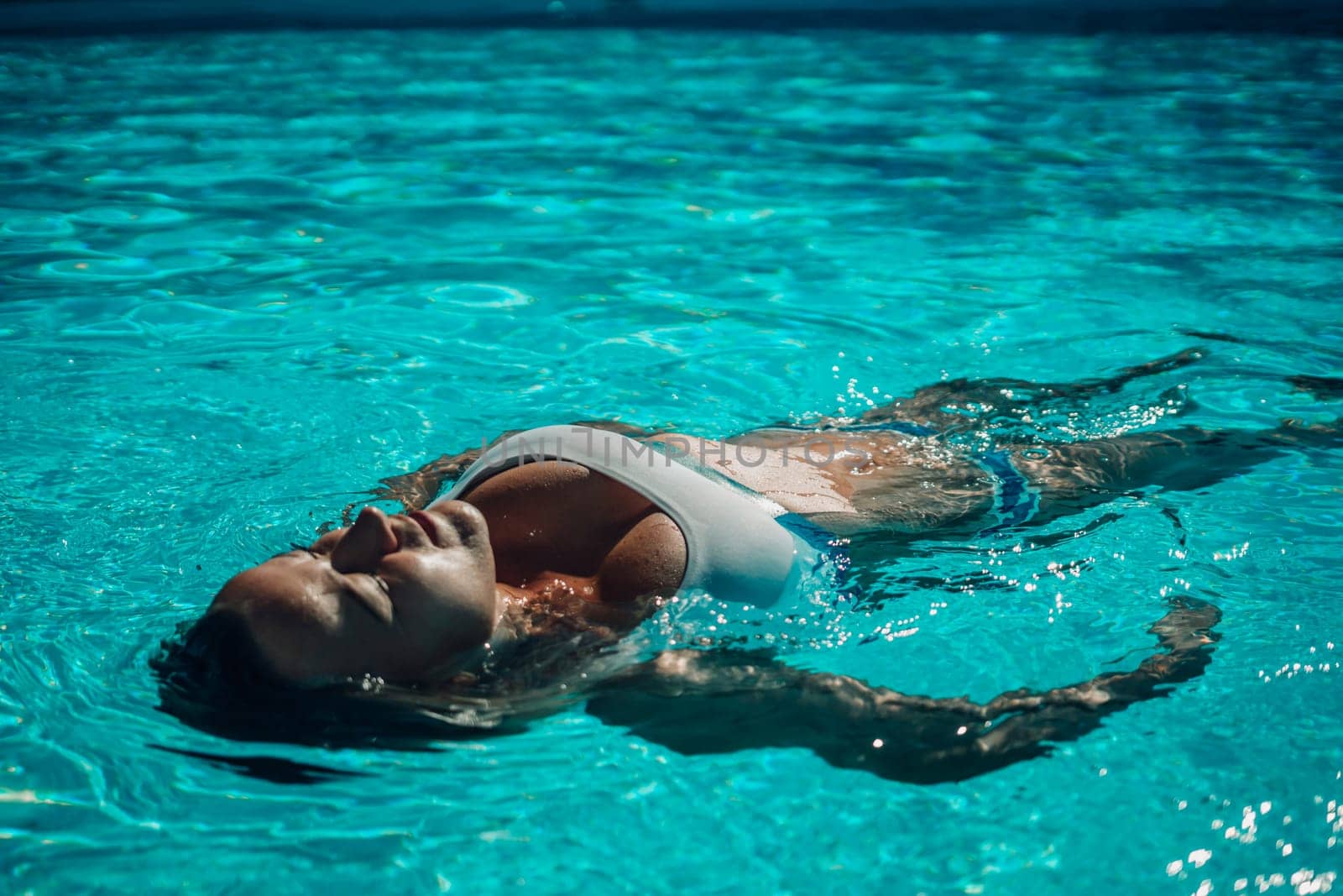 Woman relaxing swimming pool. Happy woman in a blue swimsuit floating in the pool, look form above.