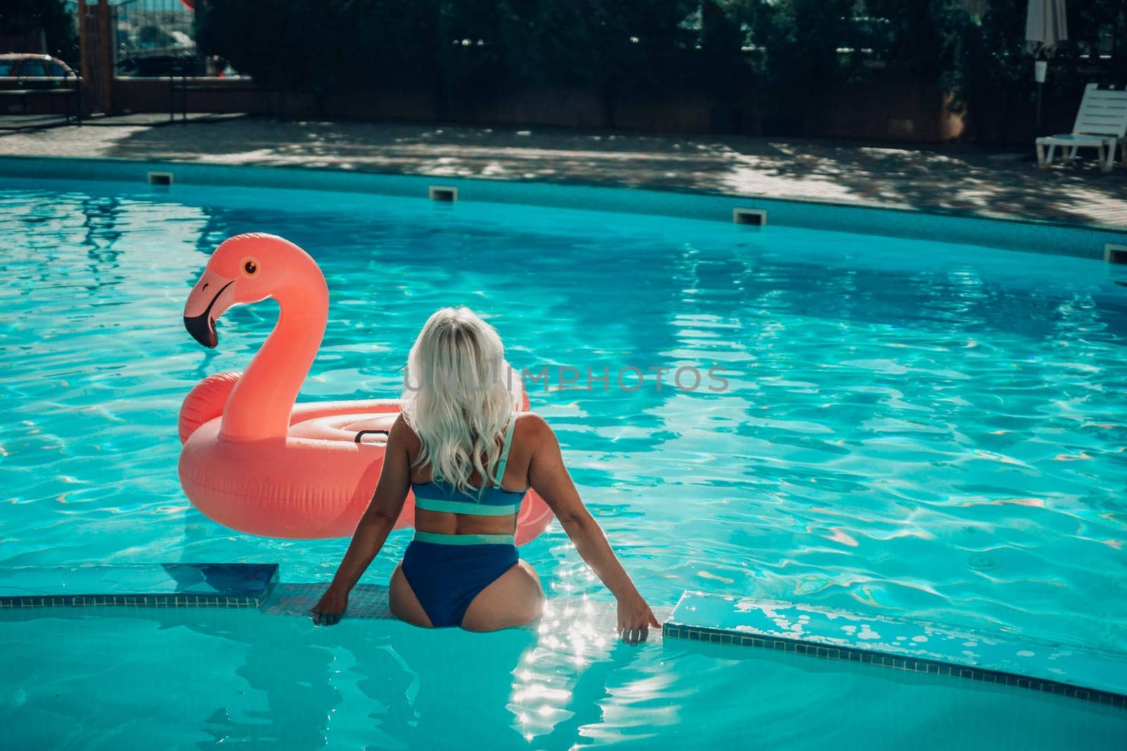 A woman in a bikini is sitting on a pink flamingo float in a pool. Concept of relaxation and leisure, as the woman enjoys her time in the water