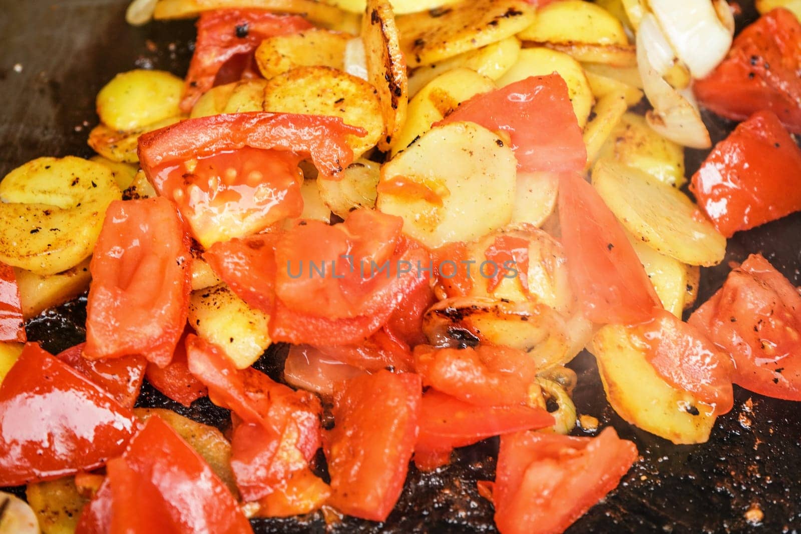 Potatoes and tomatoes cut to small pieces grilled on electric grill, closeup detail