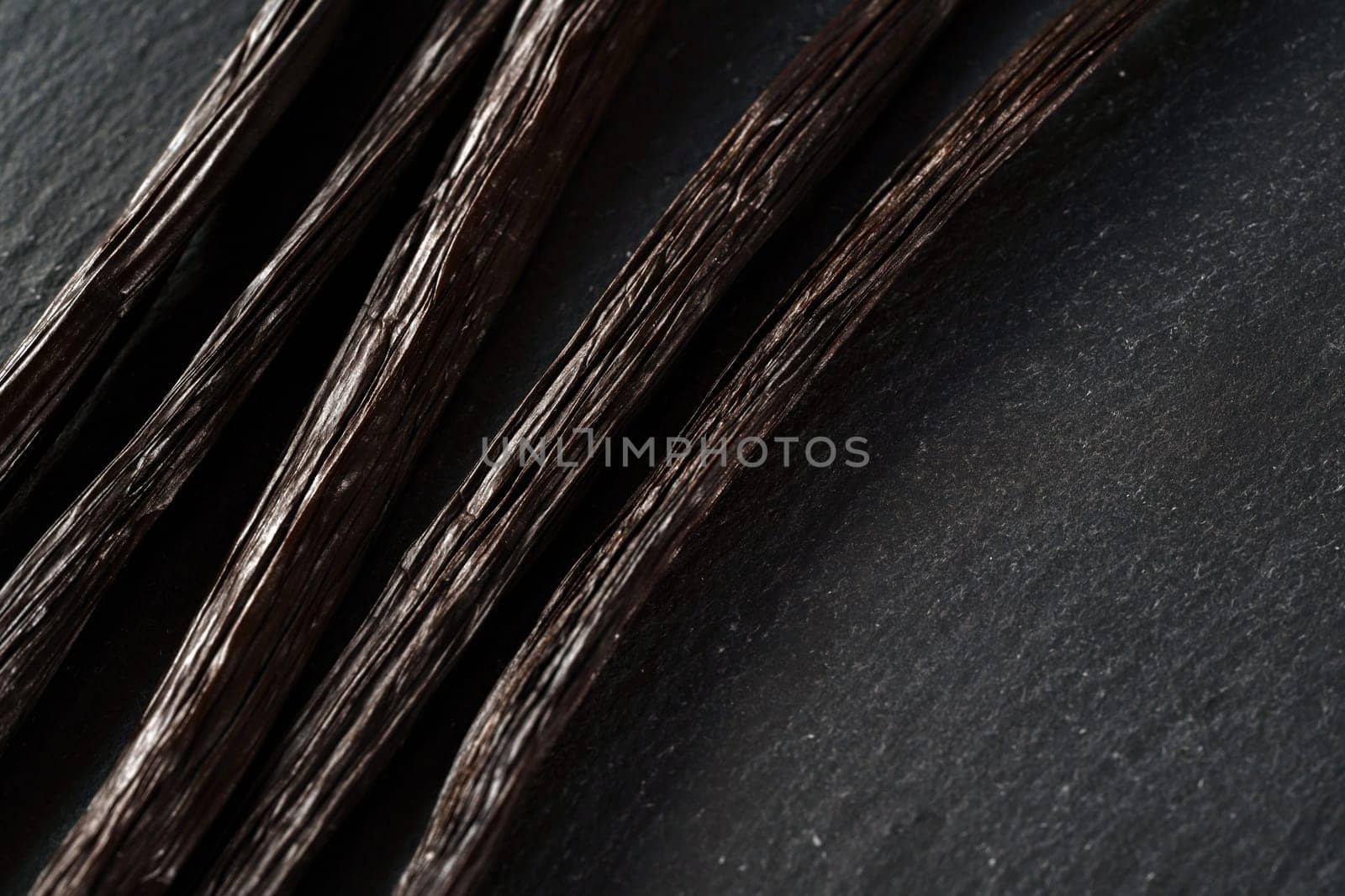Five bourbon vanilla beans on black slate desk, closeup view from above