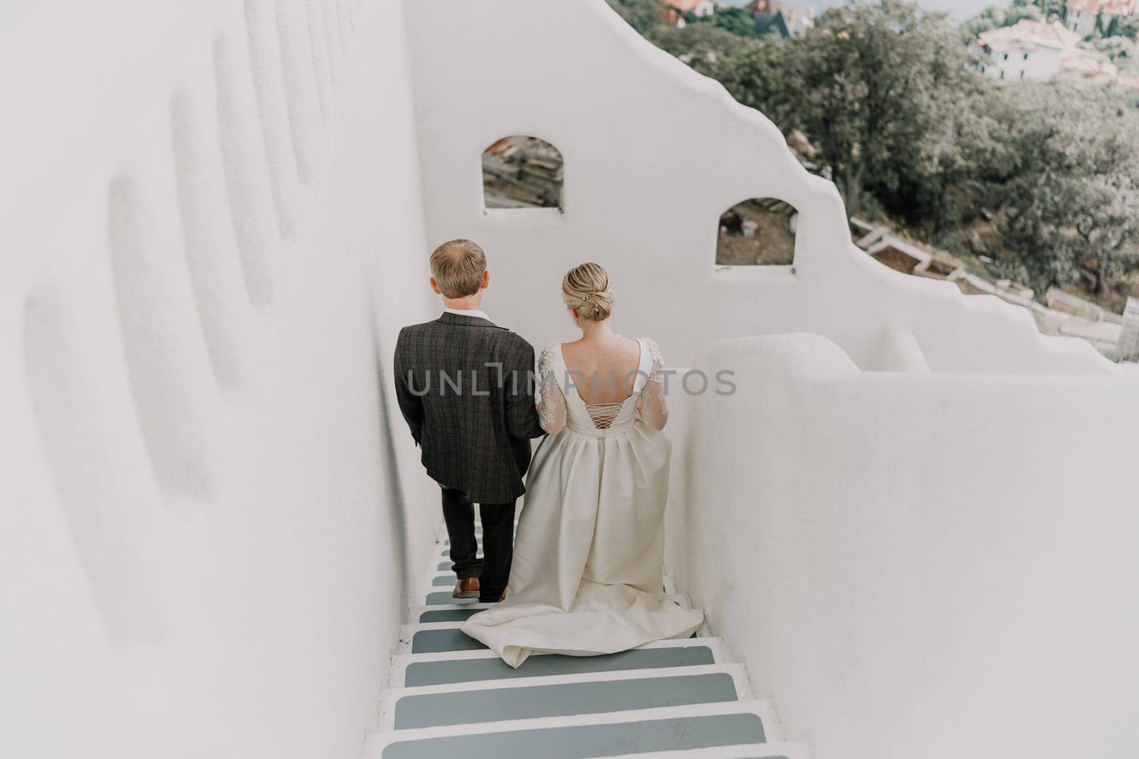 A bride and groom are walking down a white staircase. The bride is wearing a white dress and the groom is wearing a suit