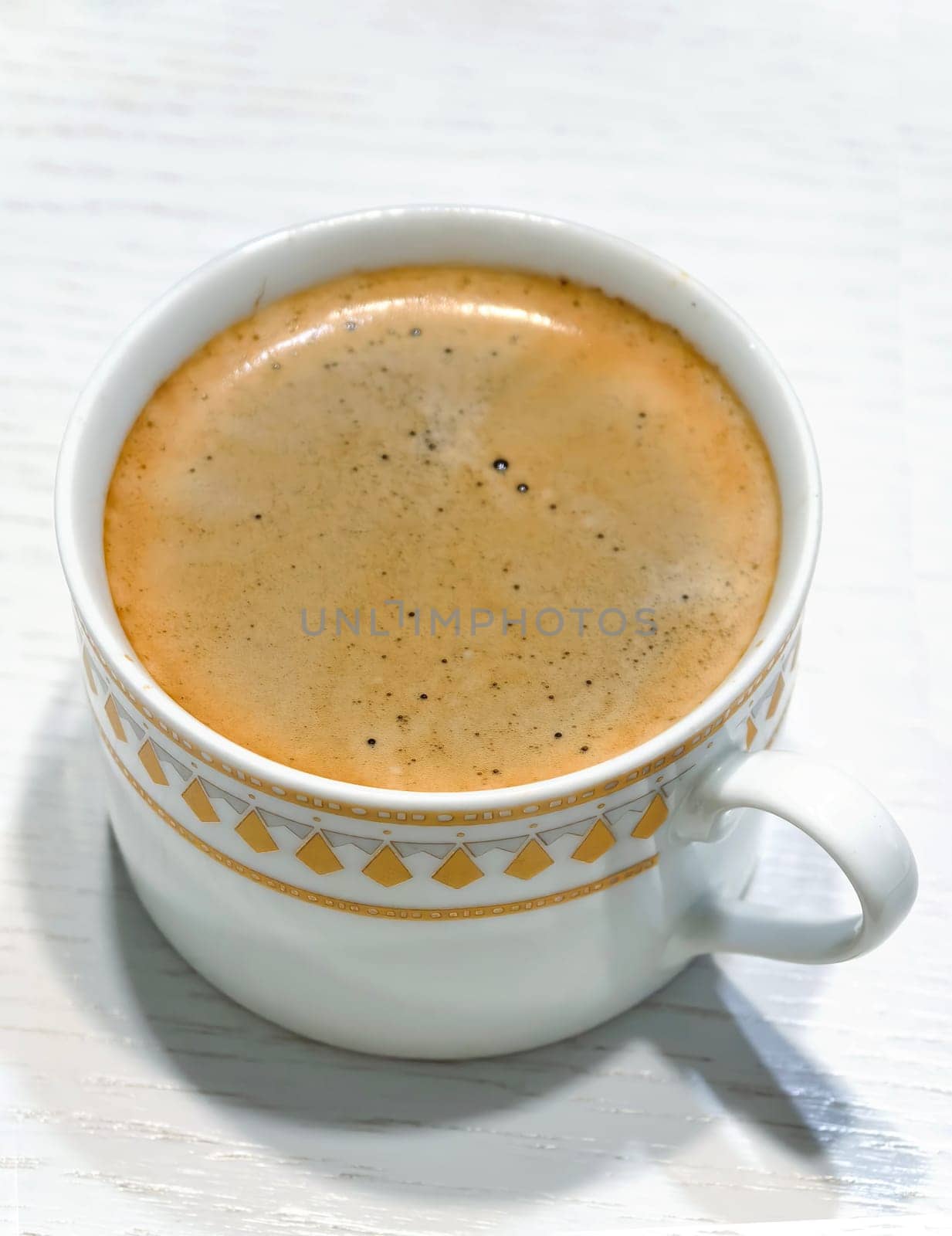 Close-up image of a freshly brewed espresso with a layer of rich, creamy foam in a decorative white cup. Photo taken with a smartphone.