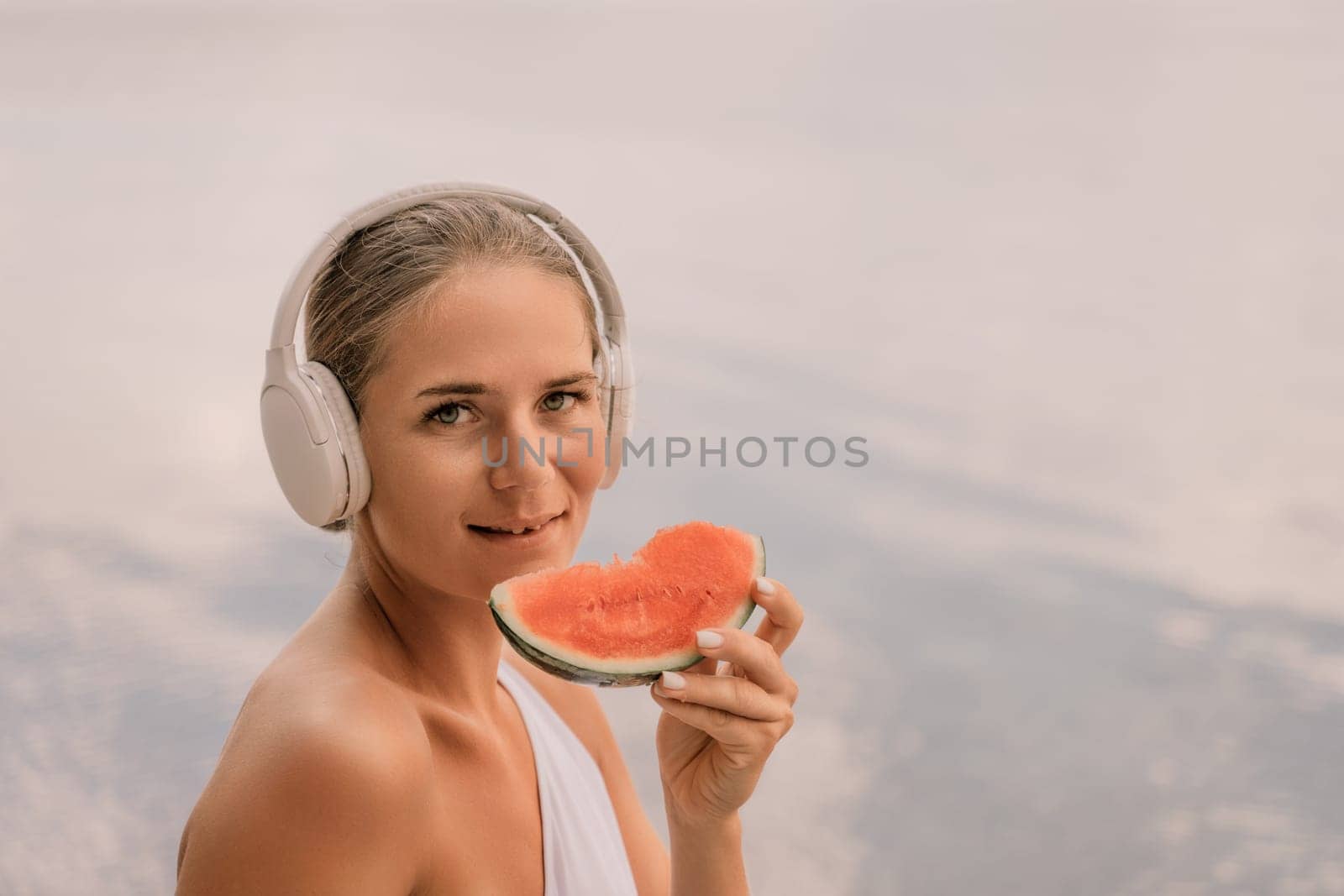 A woman is eating a watermelon slice. The watermelon is pink and green. The woman is smiling as she eats the fruit