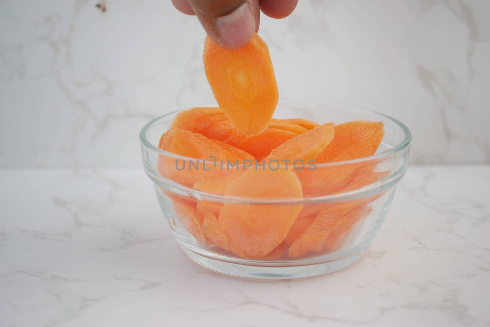 Fresh carrot slices are being lifted from a clear glass bowl.