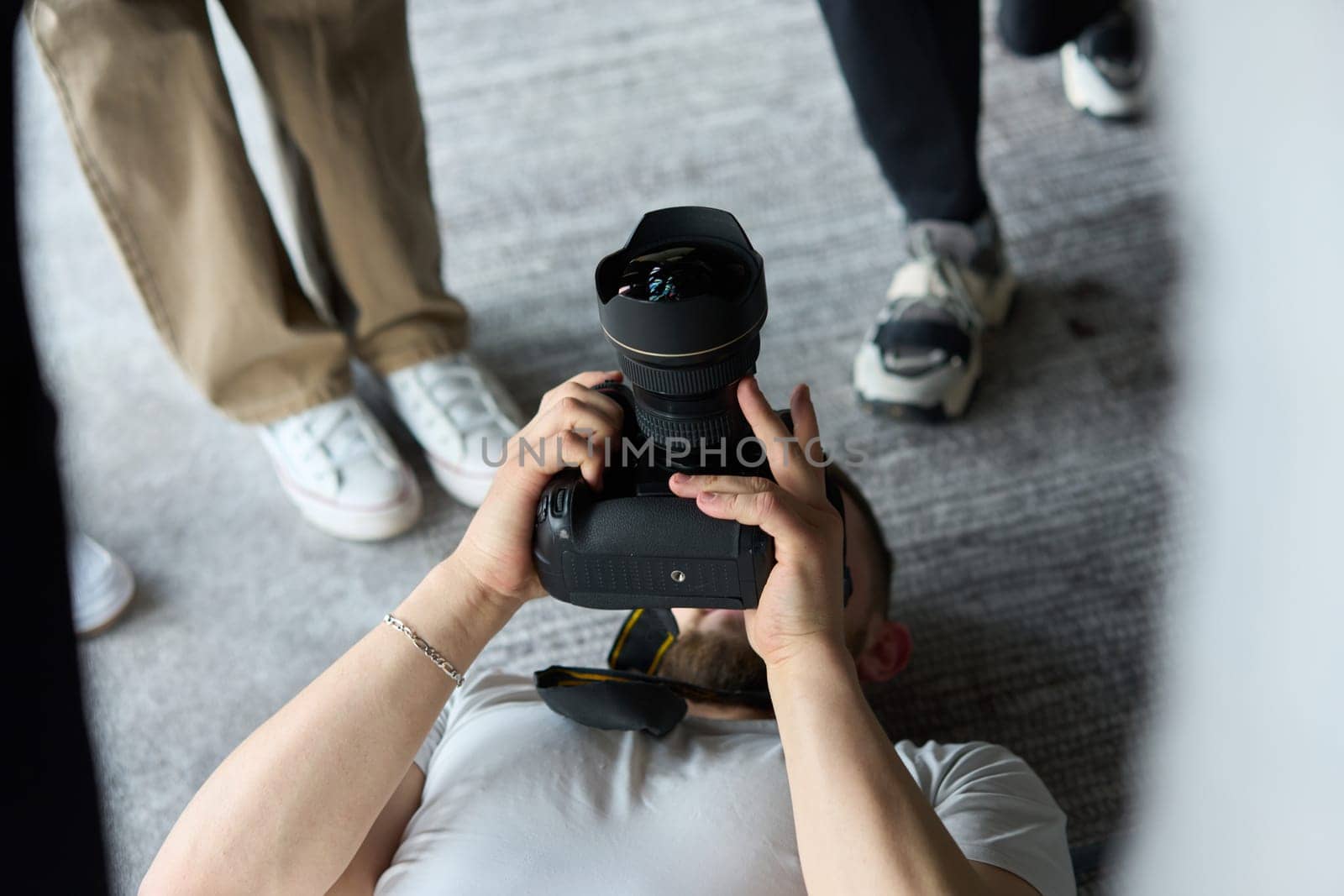 A photographer lies on the floor, capturing a heartfelt shot of a group of models embracing each other, showcasing their natural connection and joy in an intimate and creative moment.