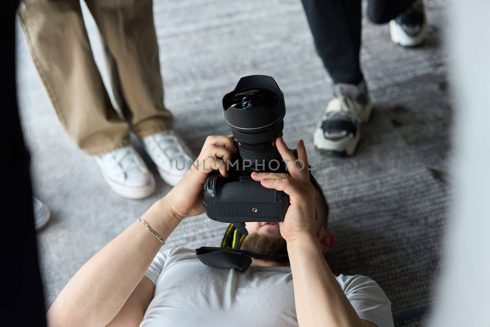 A photographer lies on the floor, capturing a heartfelt shot of a group of models embracing each other, showcasing their natural connection and joy in an intimate and creative moment.