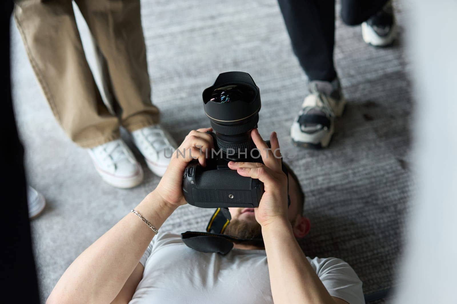 A photographer lies on the floor, capturing a heartfelt shot of a group of models embracing each other, showcasing their natural connection and joy in an intimate and creative moment.