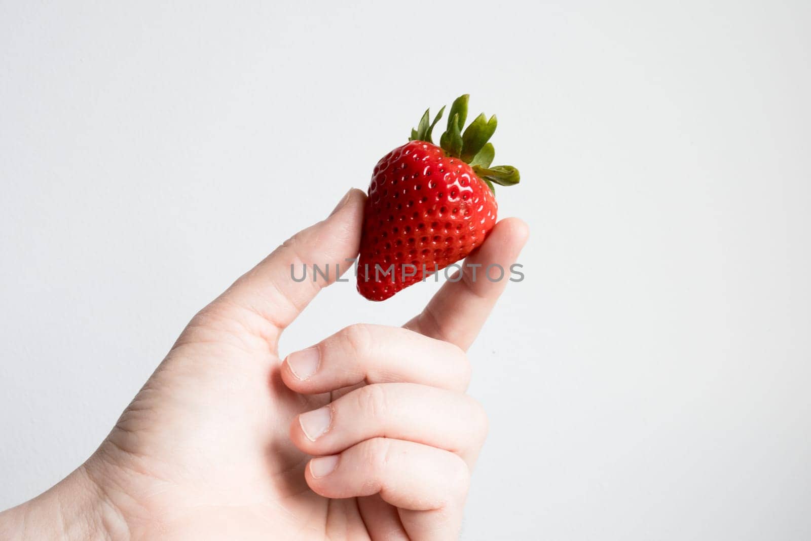 Close up of hand holding fresh strawberry against white background.