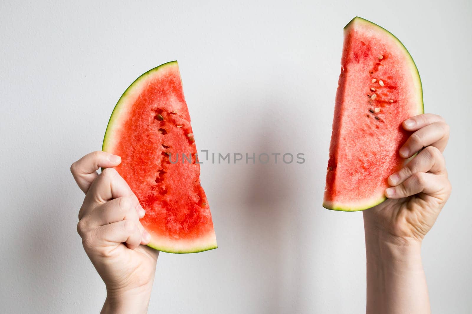 Hands holding watermelon slices against white background.