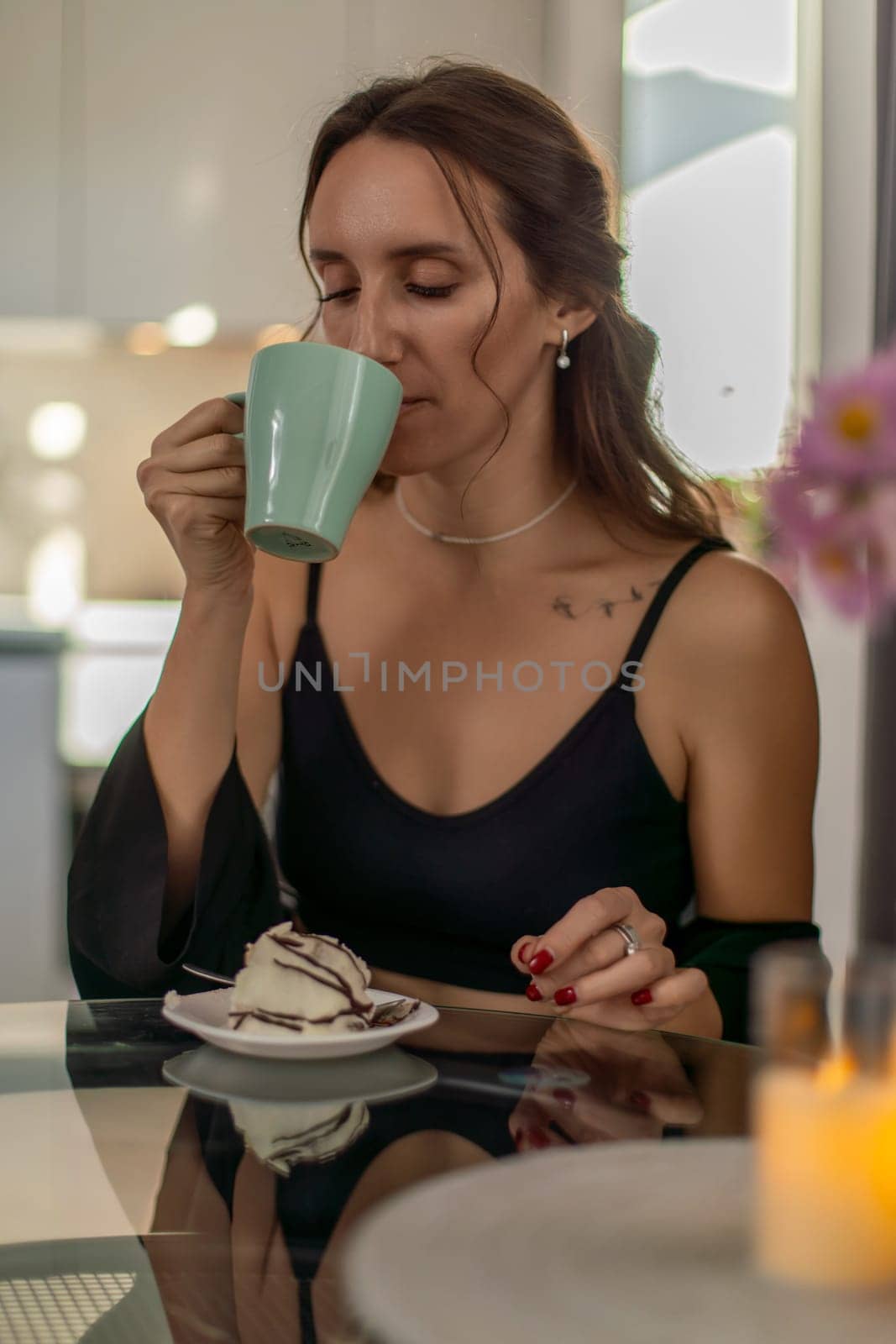 Woman with brown hair enjoys a light green mug of coffee and a pastry at a dark glass table. Ambient lighting highlights the scene.