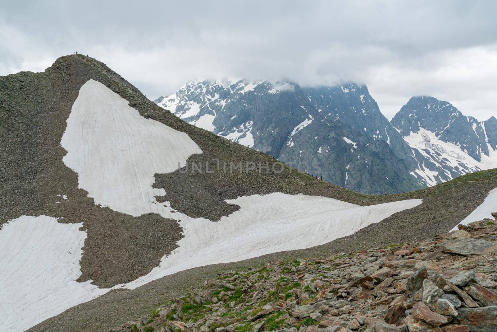 Snow-covered slopes meet rugged mountains under a cloudy sky. The scene showcases a stunning blend of natural elements, capturing the beauty of alpine terrain in an untouched wilderness.