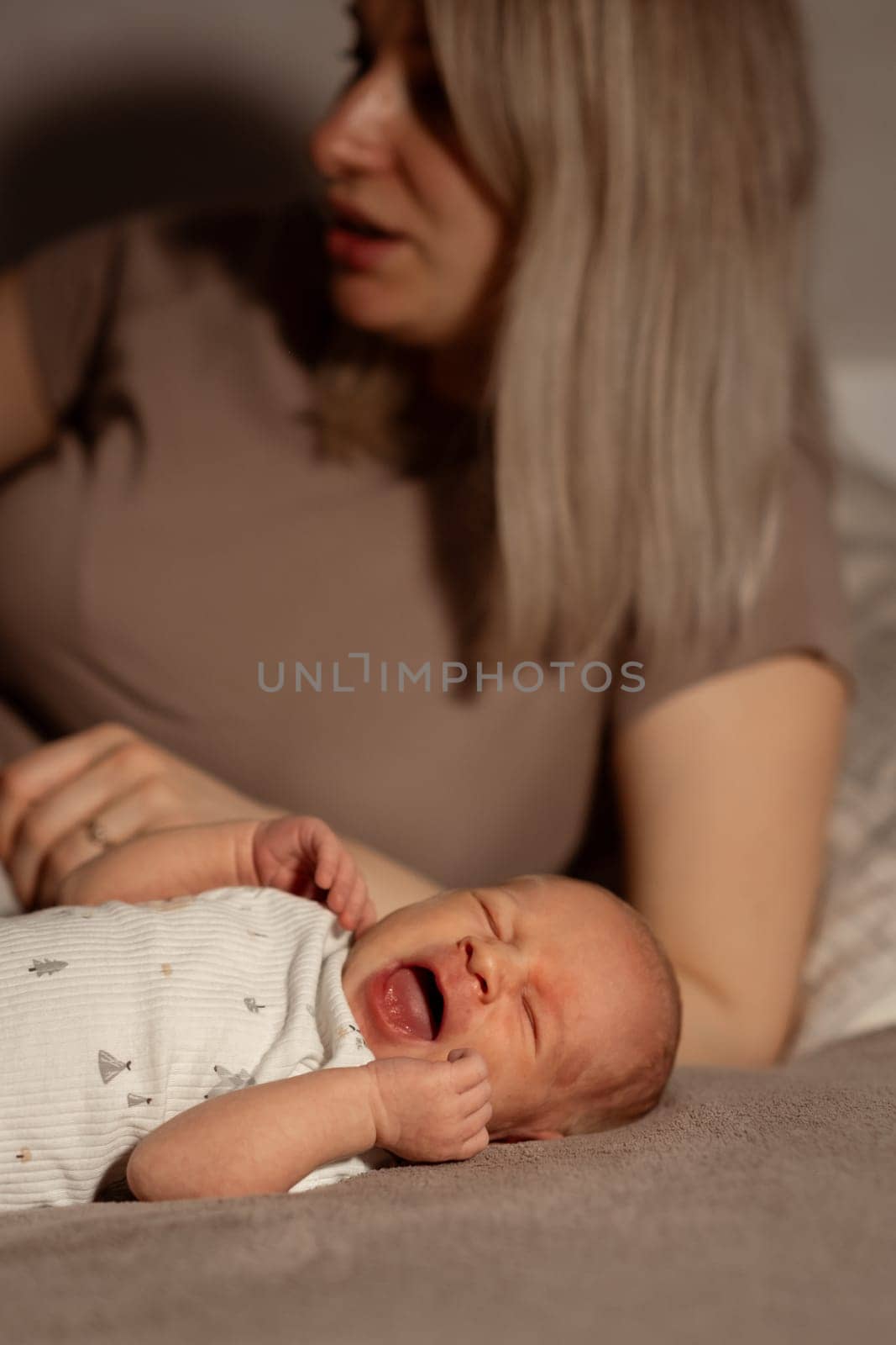 A mother lovingly holds her crying baby, providing comfort and warmth, as they enjoy a quiet moment together at home in the evening.