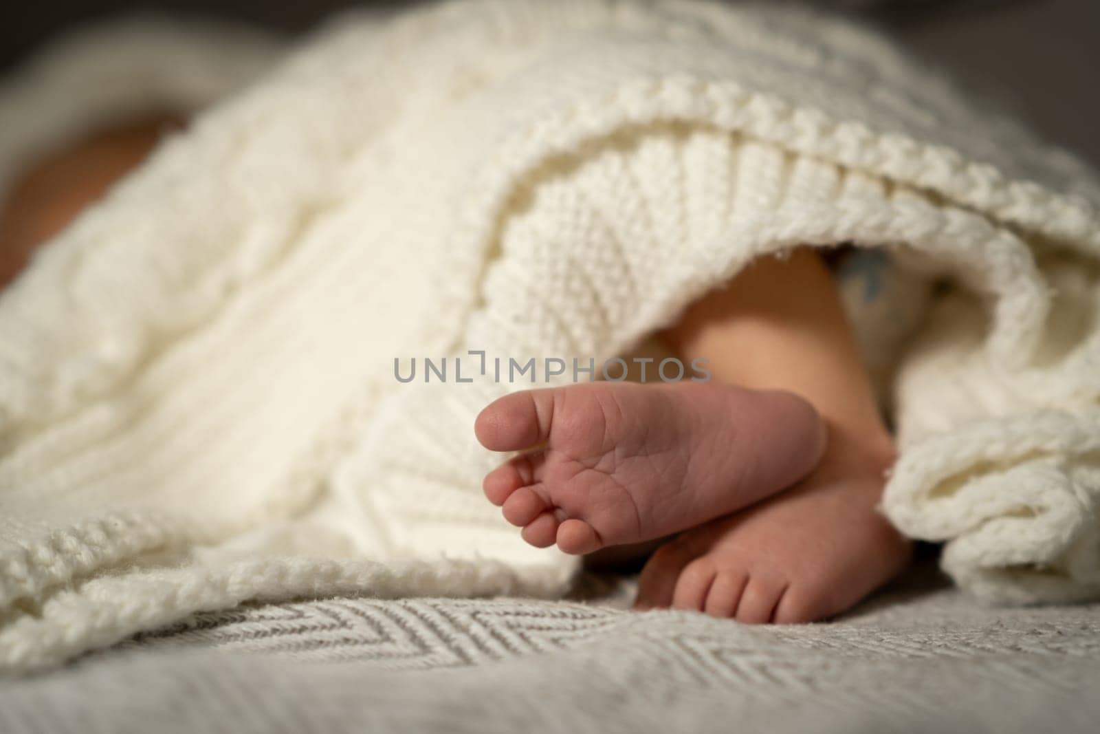 Soft baby feet are visible as the little one relaxes under a warm knitted blanket in a peaceful home setting during the afternoon.