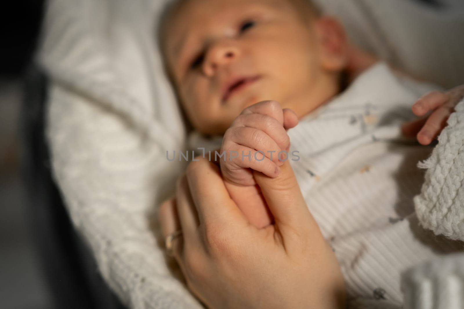 A mother cradles her babys tiny hand in a warm and intimate setting as they share a comforting moment together, reflecting love and tenderness.