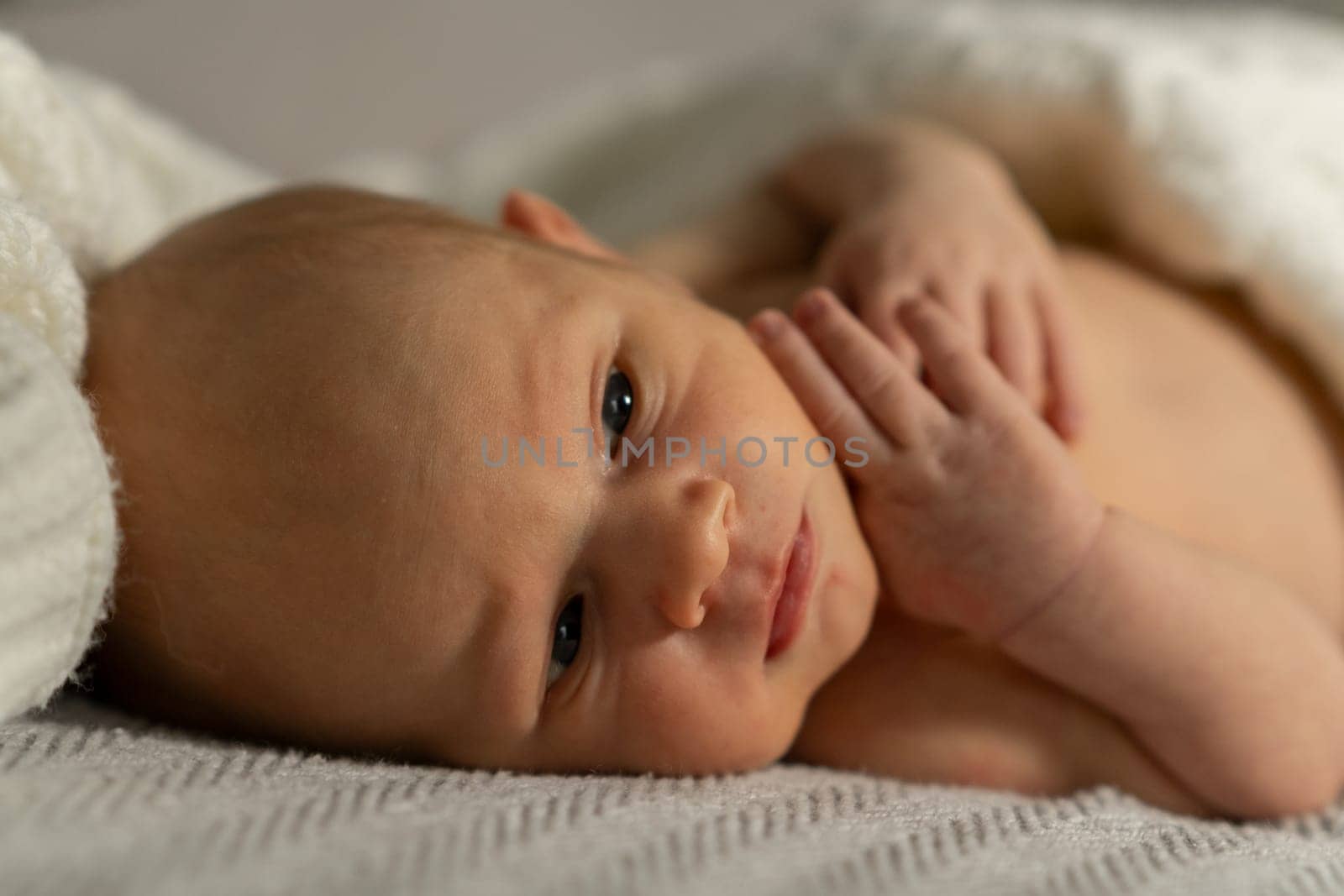 Newborn baby resting peacefully on a soft blanket with gentle lighting, displaying small fingers and an inquisitive look while enjoying a calm moment indoors