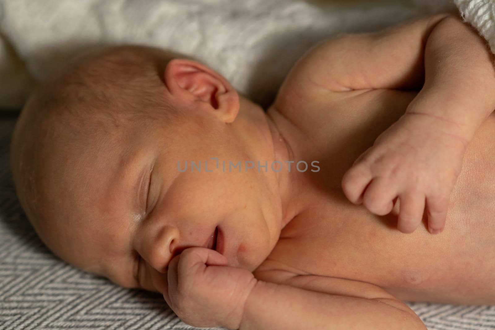 A newborn baby is gently resting with closed eyes, one hand curled near the face, showcasing innocence and tranquility in a warm living space.