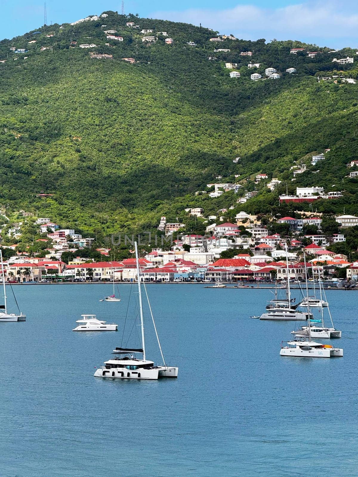 St.Thomas, part of the U.S. Virgin Islands in the Caribbean Sea 10. 28, 2023 Scenic view of sailboats anchored in a calm bay, with a hillside town of colorful houses nestled in vibrant green mountains