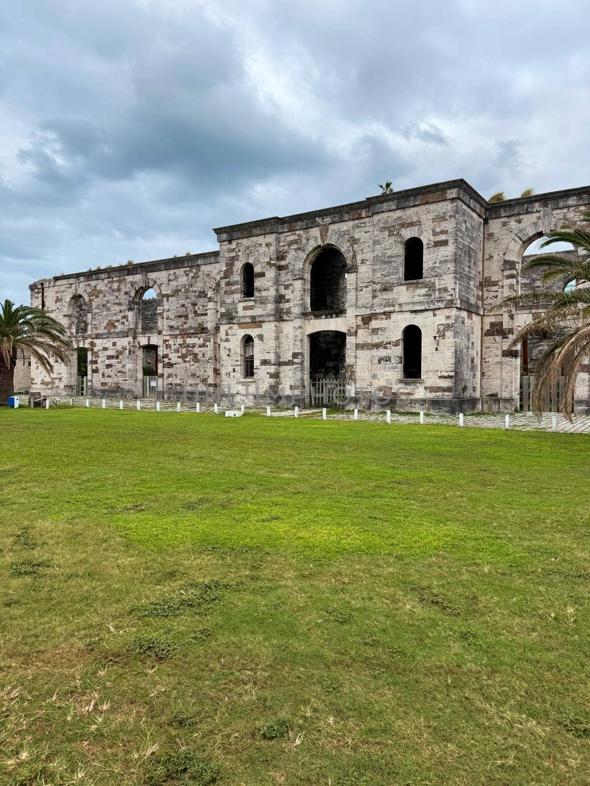Old stone ruins of a military-era building located in the Royal Naval Dockyard, Bermuda, under overcast skies and surrounded by grass.