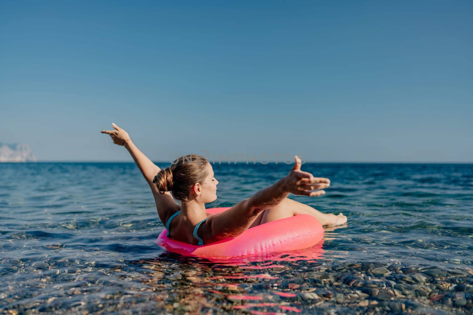 A woman is floating on a pink inflatable raft in the ocean. She is smiling and she is enjoying herself