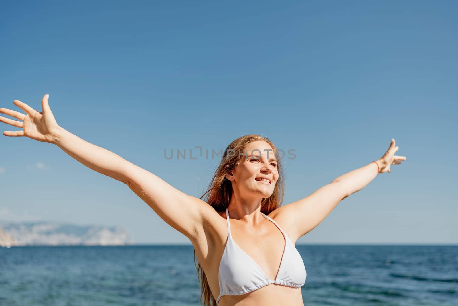 A woman in a bikini is smiling and waving at the camera. The image has a happy and carefree mood, as the woman is enjoying her time at the beach
