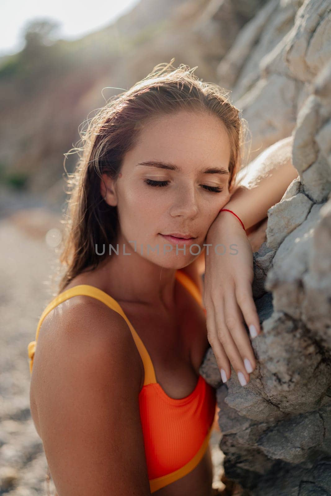 A woman in a yellow and orange bikini is laying on a rock. She has her head down and is looking away