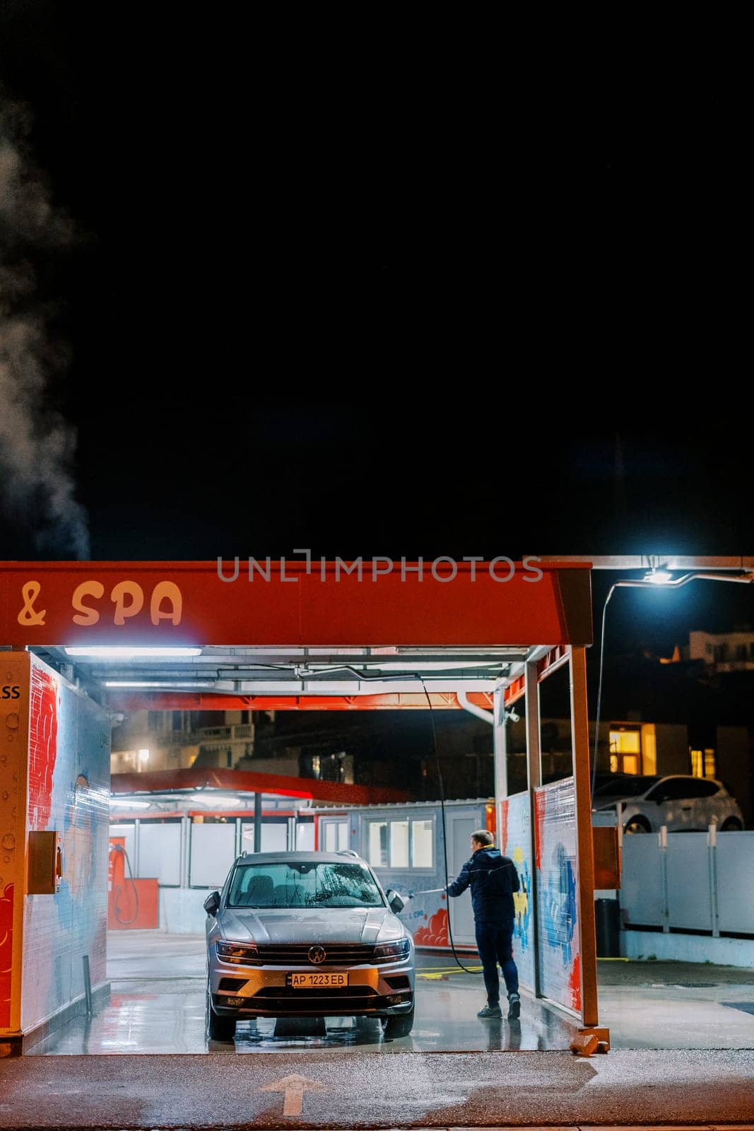 Service worker at a car wash washes a car with a hose. Back view. High quality photo