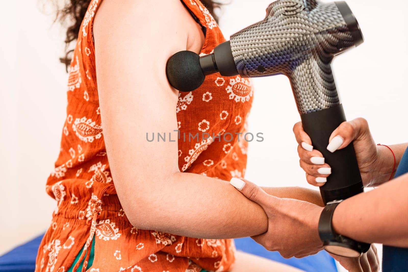 Chiropractor using massage gun on patient arm, Physiotherapist using massage gun on female patient. Percussion or vibration therapy on body