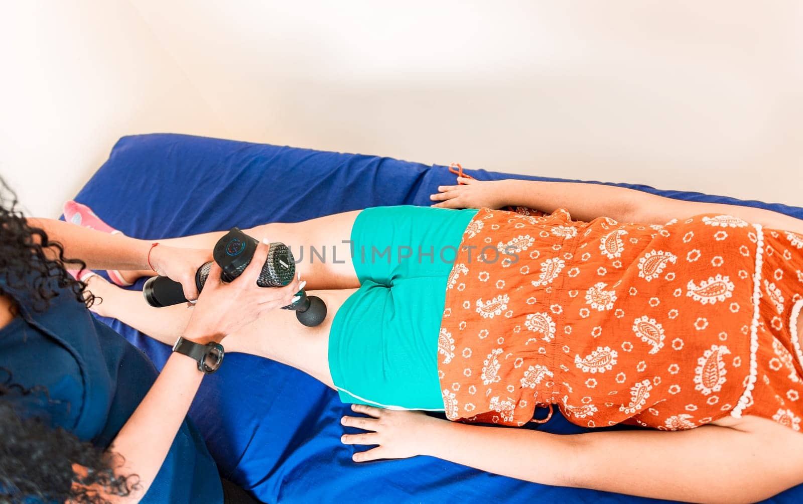 Physiotherapist using massage gun on female patient. Percussion or vibration therapy. Chiropractor using massage gun on patient leg.