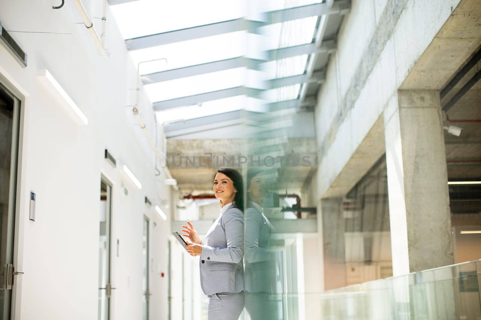 Pretty young business woman using mobile phone in the office hallway