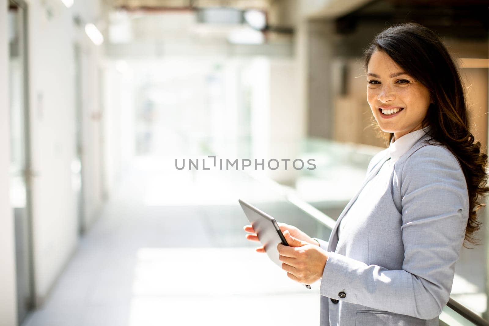 Pretty young woman working on digital tablet in the office hallway