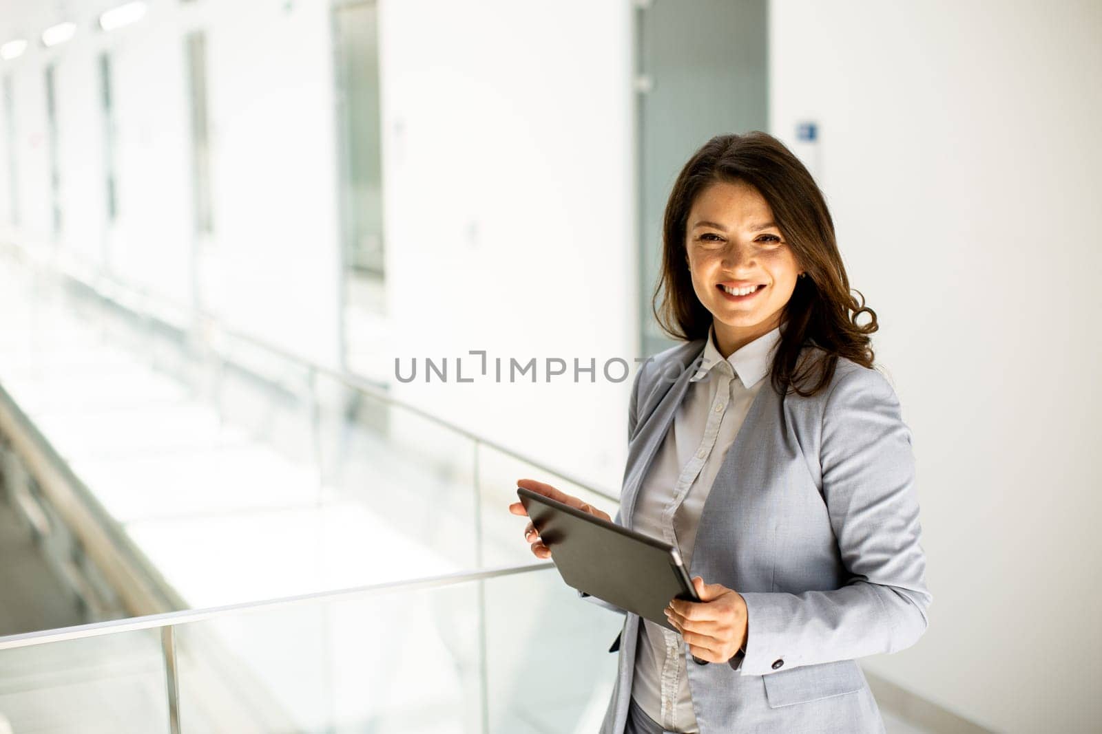 Pretty young woman working on digital tablet in the office hallway