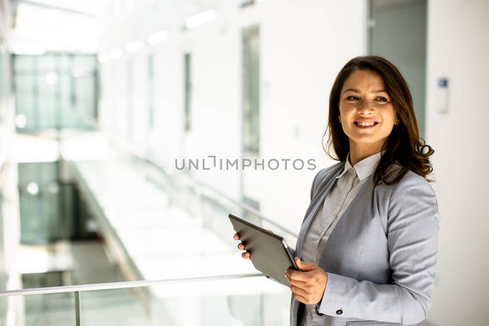 Pretty young woman working on digital tablet in the office hallway