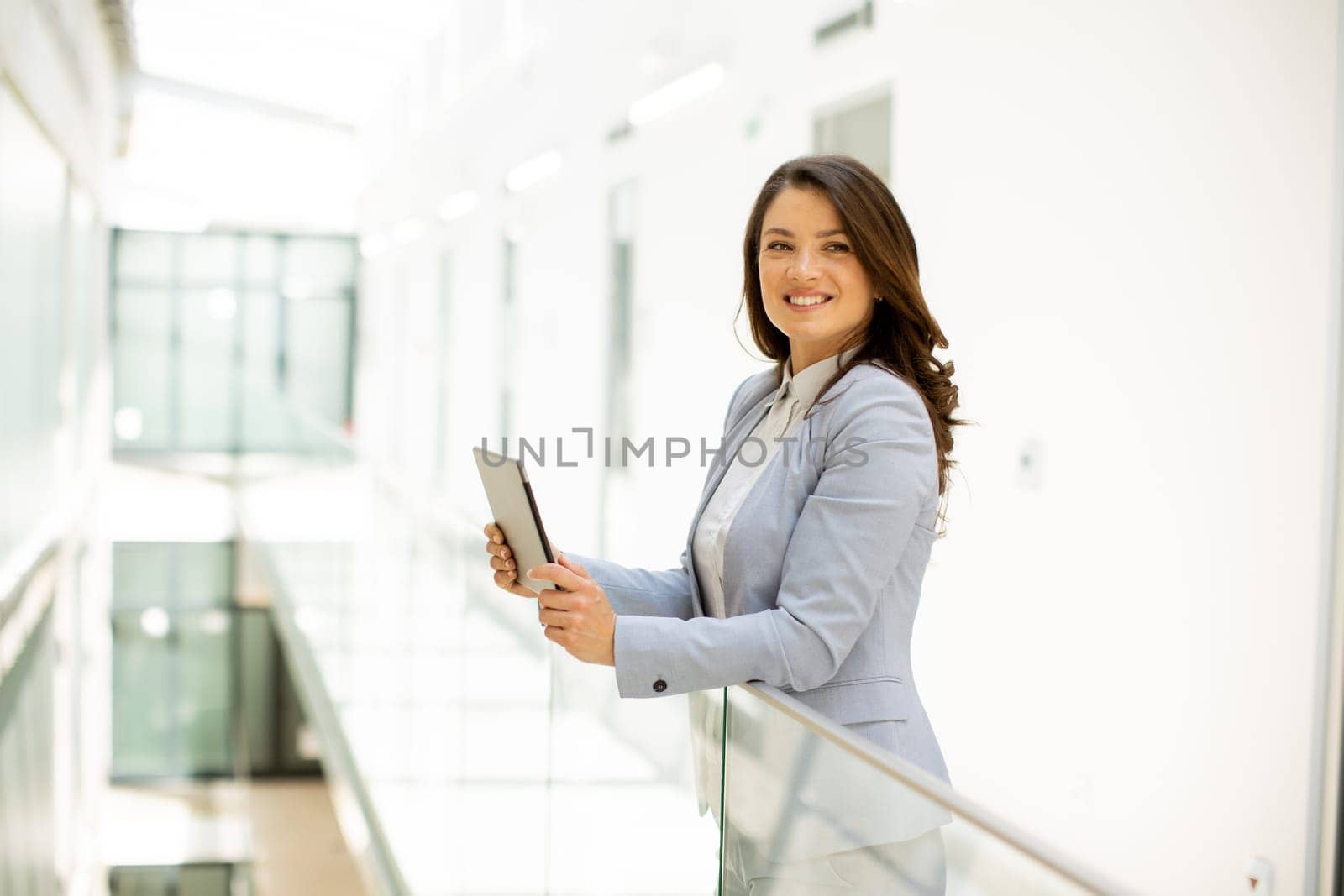 Pretty young woman working on digital tablet in the office hallway