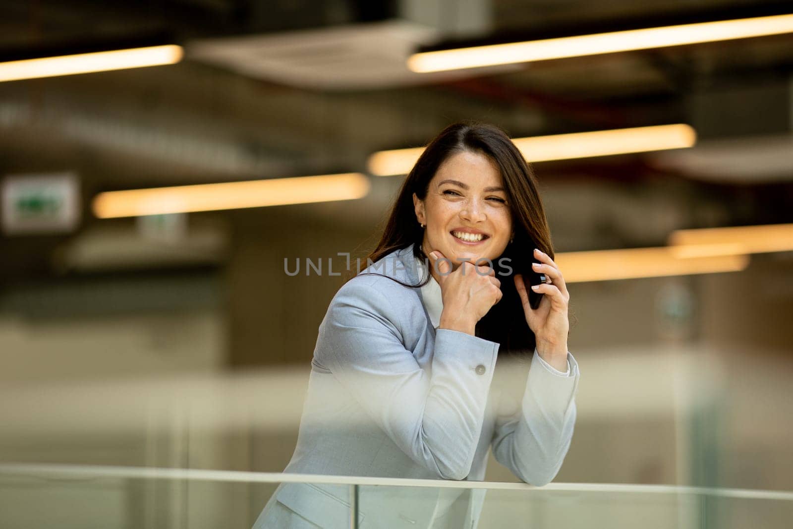 Pretty young business woman using mobile phone in the office hallway
