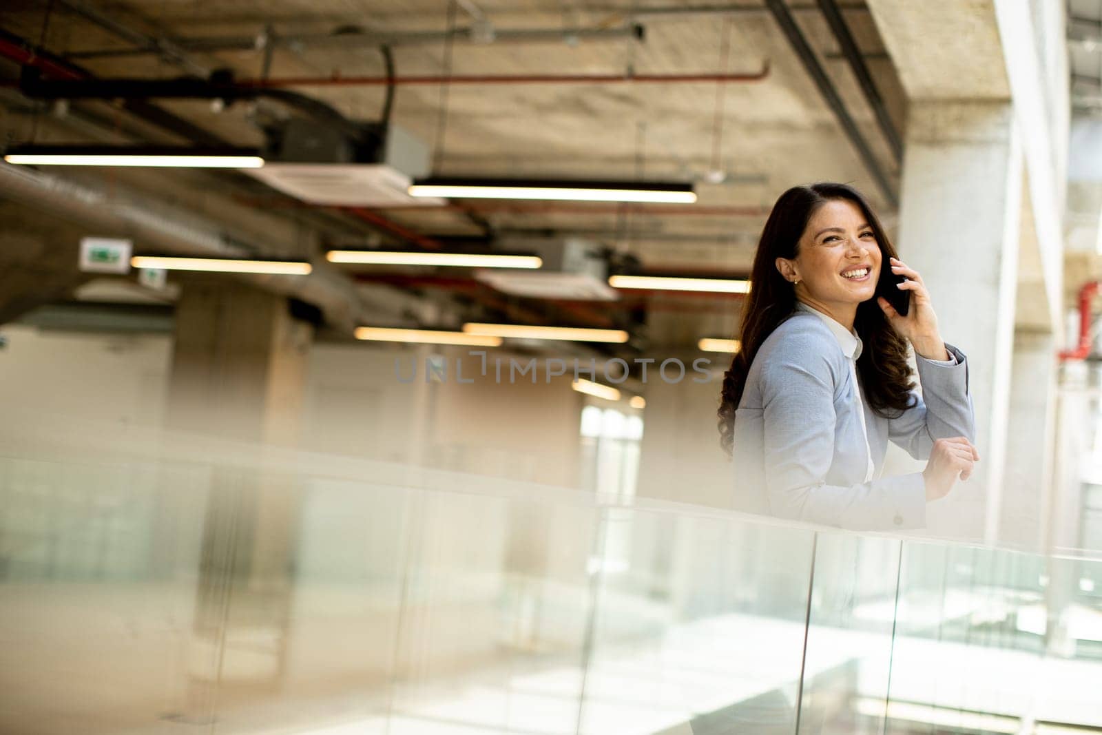 Pretty young business woman using mobile phone in the office hallway
