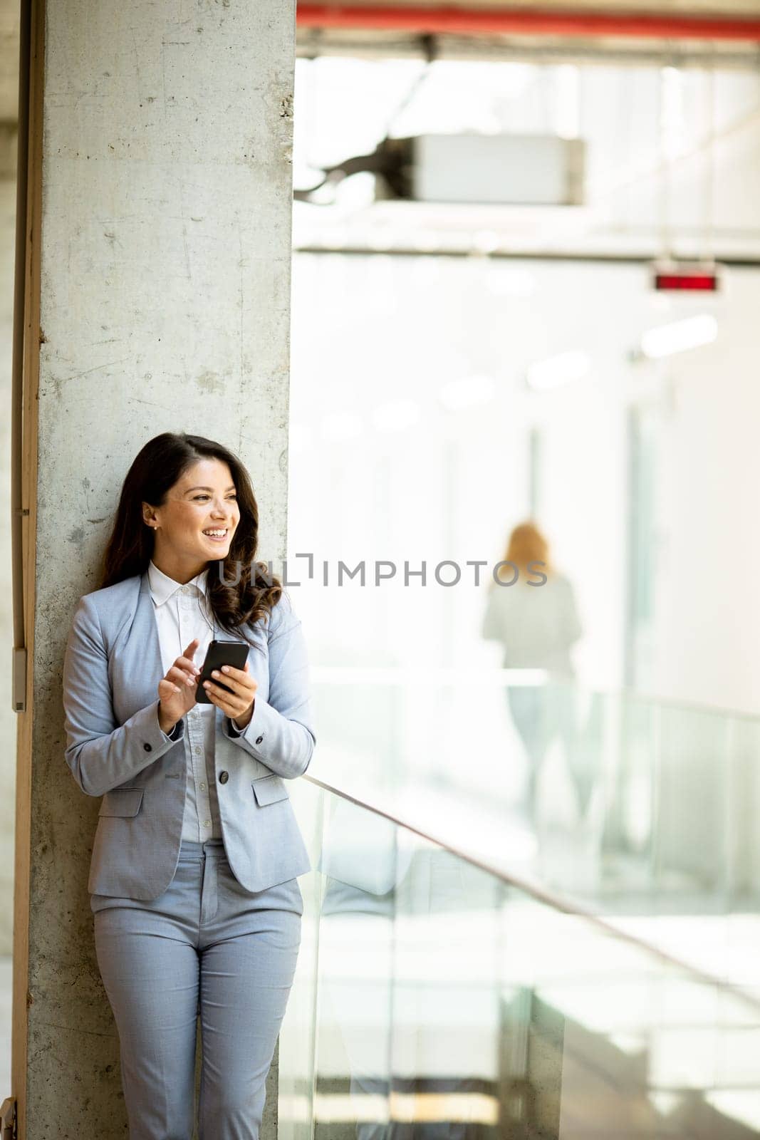 Pretty young business woman using mobile phone in the office hallway