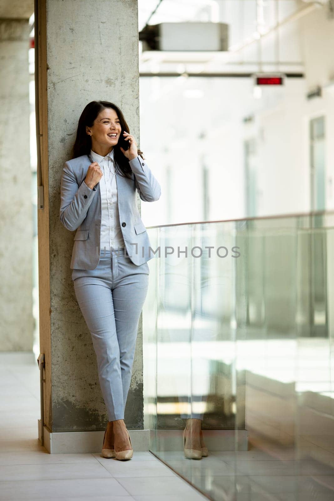 Pretty young business woman using mobile phone in the office hallway